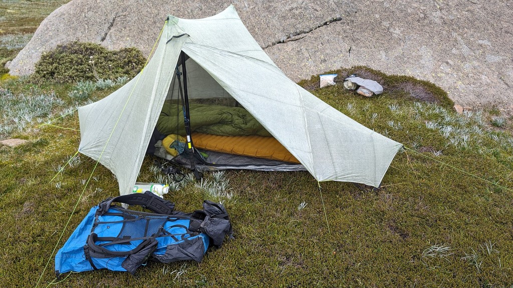 Saco de dormir y mochila junto a una tienda de campaña
